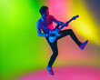 © master1305 - Jump high. Young caucasian inspired and expressive musician, guitarist performing on multicolored background in neon. Concept of music, hobby, festival, art. Joyful artist, colorful, bright portrait.