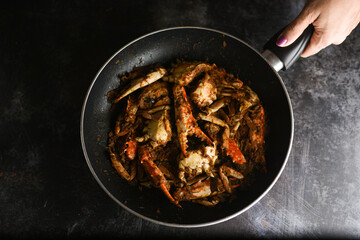 Wall Mural - Chili crab curry or Kerala crab roast popular hot and spicy seafood dish in India, Sri Lanka, Singapore. Woman hand cooking roasted coconut sauce on dark background.