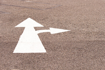 A two way arrow symbol on a black asphalt road surface.