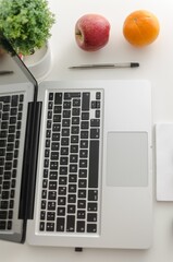 Poster - Vertical shot of a laptop with pen and fruits on a white table