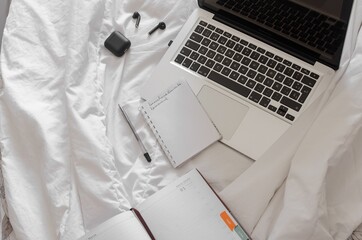 Wall Mural - Top view of a laptop with wireless earphones, pen, and notebooks on a white fabric