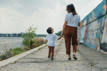 back view of mother holding hands with cute son outside