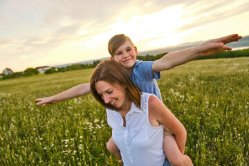 Wall Mural - happy family of mother and child on field at the sunset having fun