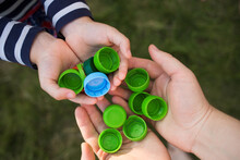 Baby Puts Plastic Lids In Mother's Hands. Parent And His Child Collect Cover. Recyclable. Collecting Bottle Caps