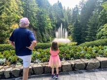 A Little Girl And Her Grandpa Admiring A Beautiful Water Fountain And Butchart Gardens, In Brentwood Bay, Vancouver Island, Canada.