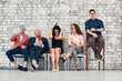 © Georgii - Group of smiling young business people sitting in line using mobile phones and other devices over white brick background