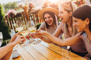 Young female friends clinking glasses with wine on the summer terrace of cafe or restaurant