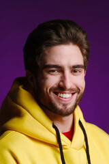 Wall Mural - A young man of 25-30 years in yellow sweatshirt emotionally poses on a purple background. 