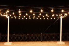 Garlands Of Lamps On A Wooden Stand On The Street. A Wedding Banquet.