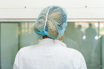 Back view on scientist working in the laboratory - Unknown caucasian woman standing in white protective coat and hat gear - new normal concept - Laboratory science testing experiment