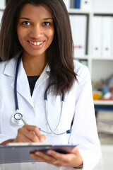 Wall Mural - Beautiful smiling black female doctor hold clipboard pad and fill something with silver pen. Physical illness prevention prescribe remedy ward round therapeutist assistance healthy lifestyle concept