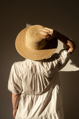 Wall Mural - Young pretty woman in straw hat and white dress / sundress. Sunlight shadow on the wall. Minimal fashion design concept.