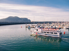 Pleasure Boat Sailing Through The Modern Marina Of Laredo At Sunset With The Peña De Santoña In The Background