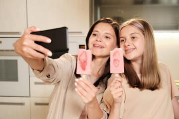 Poster - Two young cheerful females with homemade icecream making selfie in the kitchen