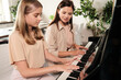© pressmaster - Cute teenage girl with long blond hair sitting by piano next to her mother