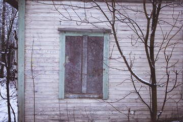 Poster - Closeup of a window of an old abandoned house surrounded with leafless trees in winter