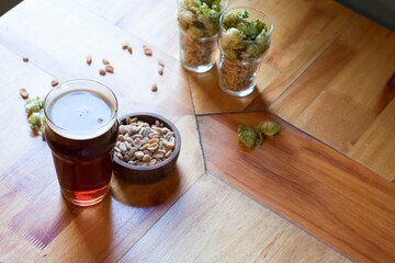 Sticker - High angle shot of a glass of beer next to peanuts, pine nuts, and hops on a wooden surface