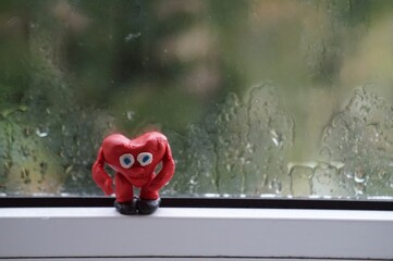 Sticker - A red heart made of plasticine on a wet window.