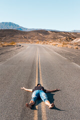 Wall Mural - A woman lying barefooted on an empty road in the Death Valley