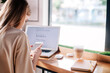 © Denis - Young girl with phone in hand works behind a laptop in a coffee shop and drinks a cappuccino