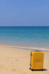 Wall Mural - Yellow tourist suitcase on the beach near the blue water.