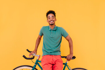 Joyful black cyclist laughing to camera. Handsome african young man posing with pleasure near his bicycle.