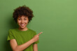 © WHstudio Leushin N - Friendly looking glad female shop assistant happy to help customers, shows way and demonstrates discounts in shop, points fore finger aside on empty space over green background. Advertising concept