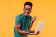© Look! - Handsome male freelancer in glasses smiling on yellow background. Ecstatic african student holding laptop and expressing happiness.