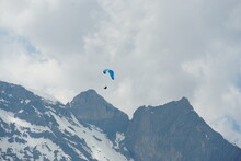 A Paraglider Gliding Over Mountain Peaks In Region Engelberg Canton Obwalden In Switzerland In The Spring When The Slopes Of The Alps Are Still Covered With Snow.