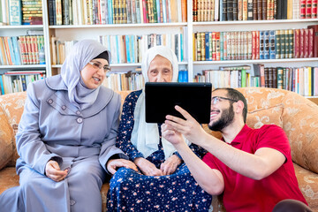 Wall Mural - Happy arabic family sitting on sofa and using technology