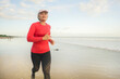fit and happy middle aged woman running on the beach - 40s or 50s attractive mature lady with grey hair doing jogging workout enjoying fitness and healthy lifestyle