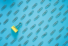 Yellow Paper Clip Laid Among Steel Paper Clip On Blue Background , Differentiation Concept