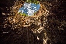 View From Below Of Blue Sky With White Clouds From The Sinkhole In The Caucasus. High Rocky Walls Of The Underground Cave.