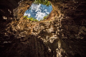 View from below of blue sky with white clouds from the sinkhole in the Caucasus. High rocky walls of the underground cave.