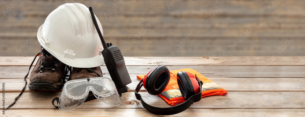 Work safety protection equipment. Industrial protective gear on wooden table, blur construction site background. - obrazy, fototapety, plakaty 