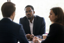 Serious African Businessman In Formal Suit And Glasses Listens Speaker During Group Meeting, Diverse Businesspeople Attending At Negotiations Solve Issues Offer Solutions, Consider Trade Opportunities