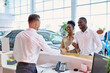 © alfa27 - auto business. friendly caucasian manager greeting dark-skinned customers in car salon