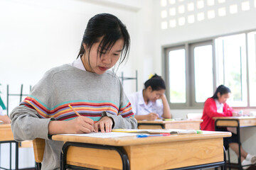 Wall Mural - Woman Young Asian students group writing test paper answer sitting on taking final examination in classroom with concentration, Test in high school /university student in exam room concept