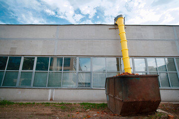 Yellow garbage chute loaded dumpster in front of old factory under construction. Loaded dumpster near construction site, renovation. Safe waste disposal.