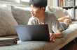 © ersp - Young asian man work form home using laptop on sofa
