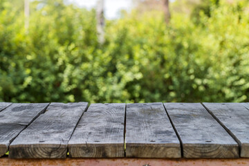 Grey wooden picnic table top at sunny summer day on blurred background of green bushes