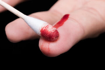 Wall Mural - Use a cotton swab to wipe the blood at the wound on fingertips that are bleeding on dark background.