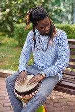 Dark-skinned African Musician Plays On Drums Outdoors, Man Enjoys Performing Music. He Sits On Bench And Play