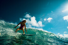 Professional Surfer Girl Riding Wave On Surfing Board Under Bright Sun On Background.