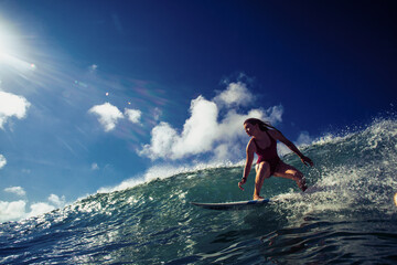 Wall Mural - professional surfer girl riding wave on surfing board under bright sun on background.