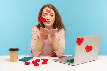 Love you! Amazing woman with kind expression sitting at workplace office, all covered with sticker hearts, sending romantic sensual air kiss, expressing romantic feelings. indoor studio shot isolated