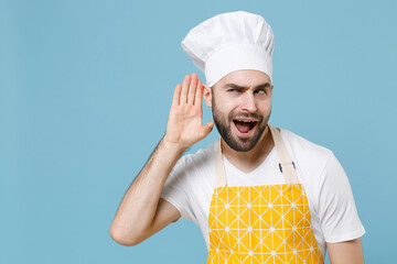 Shocked young bearded male chef cook baker man in apron white t-shirt toque chefs hat isolated on blue background studio. Cooking food concept. Mock up copy space. Try to hear you listening intently.