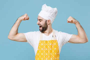 Wall Mural - Strong young bearded male chef or cook baker man in apron white t-shirt toque chefs hat isolated on pastel blue background studio. Cooking food concept. Mock up copy space. Showing biceps, muscles.