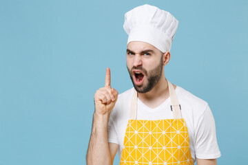 Wall Mural - Angry young bearded male chef or cook baker man in apron white t-shirt toque chefs hat isolated on blue background studio portrait. Cooking food concept. Pointing index finger up screaming swearing.