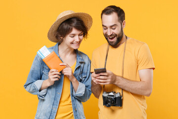 Wall Mural - Funny tourists couple friends guy girl in summer clothes isolated on yellow background. Passenger traveling abroad on weekends. Air flight journey concept. Hold passport tickets using mobile phone.